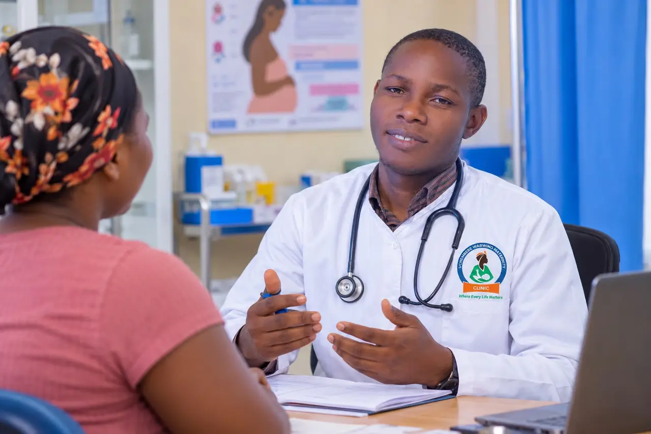 A clinician in a white coat talking with a patient across his desk