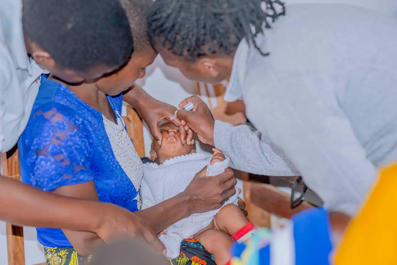 A health worker giving a baby oral vaccine drops while the mother holds the baby