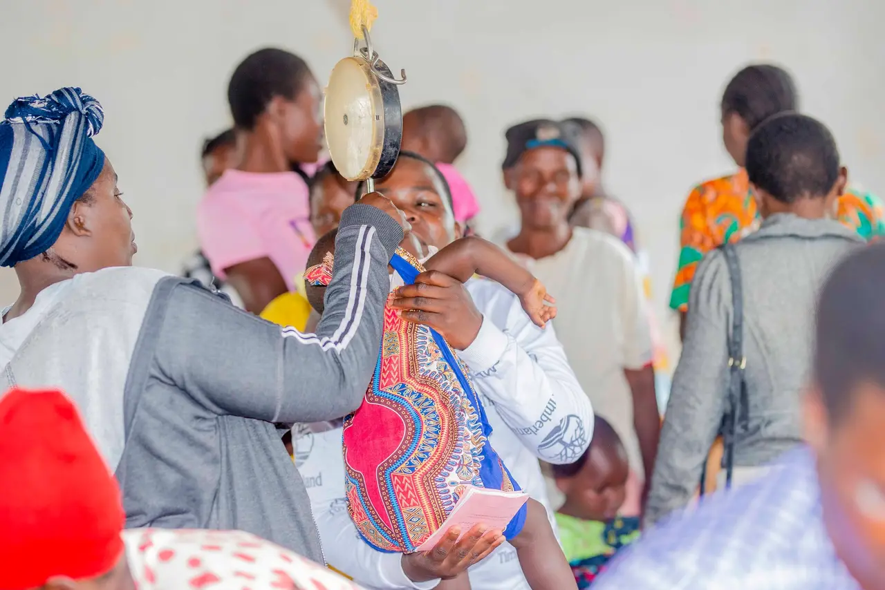 An outreach team member weighing a child in a sling scale at a monthly outreach clinic