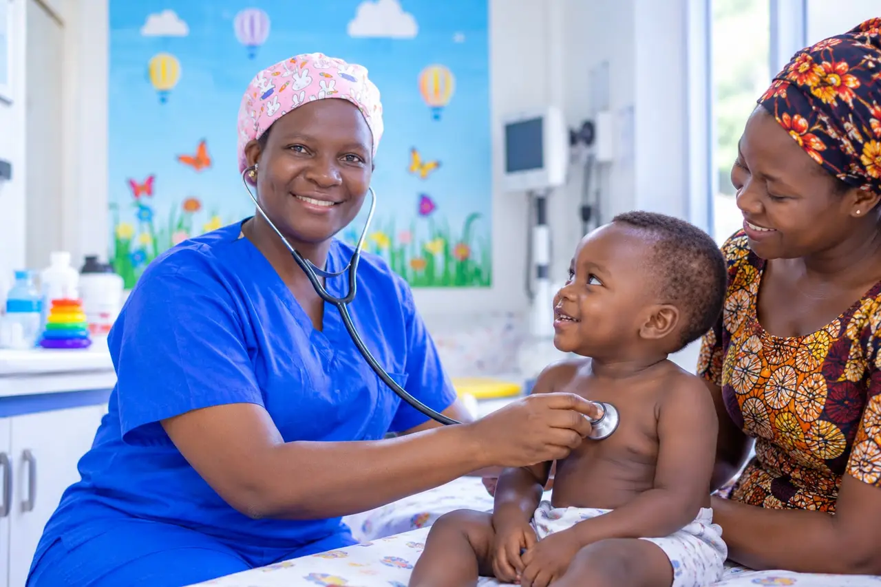 A nurse listening to a smiling baby’s chest with a stethoscope while the mother holds the child