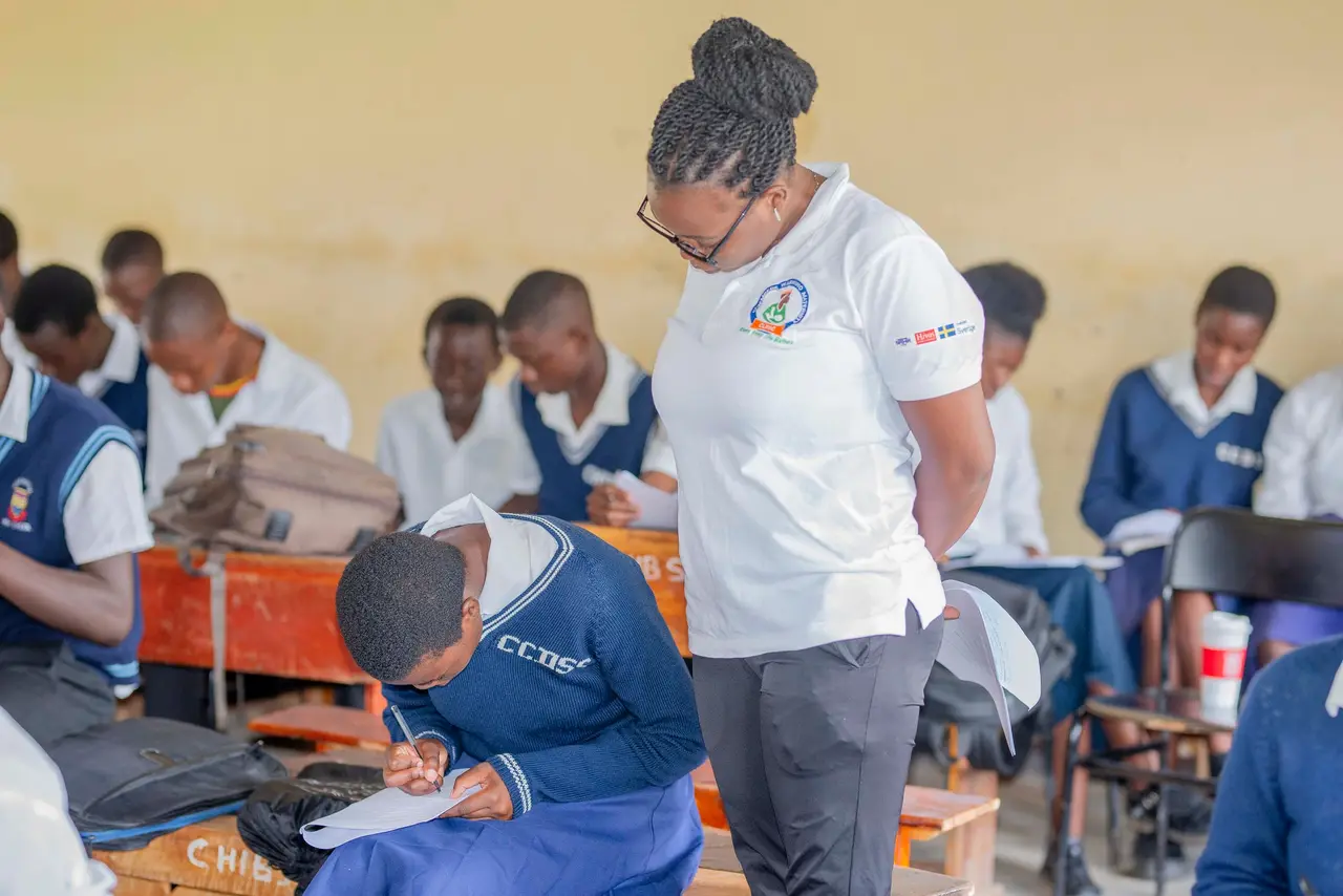 A facilitator in an Uchembere Wabwino shirt guiding secondary school learners during a lesson
