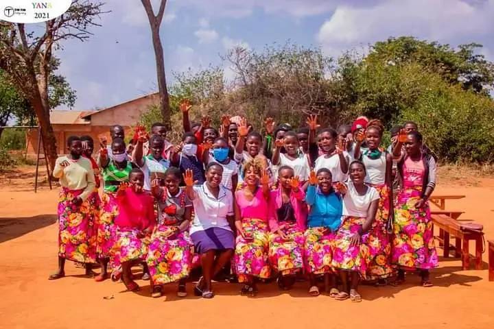 A large group of girls in colourful wrappers posing outdoors at Dunduzu Yana