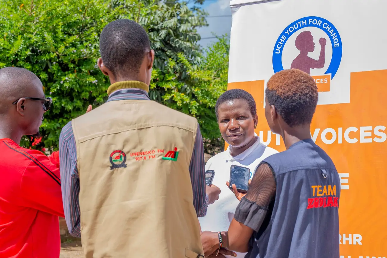 Young people holding up phones to record an interview with a woman in front of an Uche Youth for Change banner